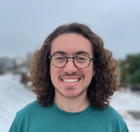A headshot of me, a white man with shoulder-length, curly brown hair and some facial hair. I am wearing glasses and a green t-shirt and smiling into the camera.